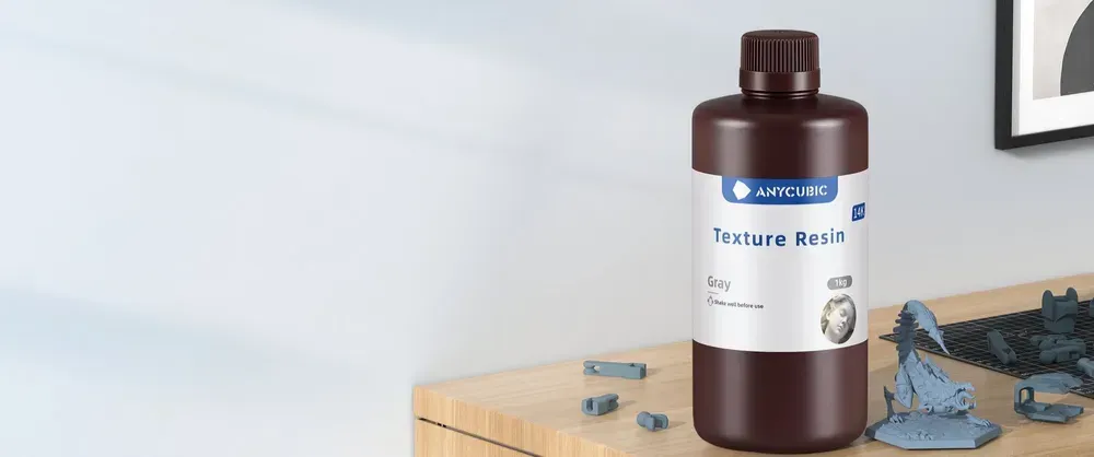 Флакон 1 кг смолы Anycubic 14K Texture Resin серого цвета на столе рядом с напечатанными моделями